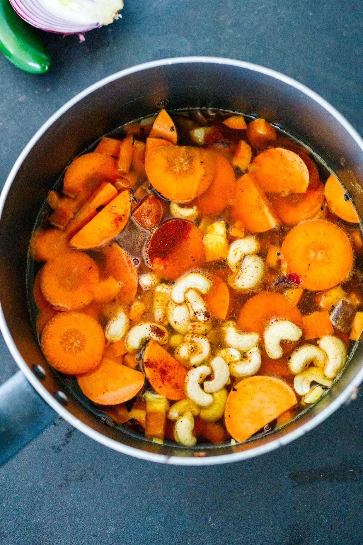 sliced orange veggies and cashews in pot with water to make vegan queso.