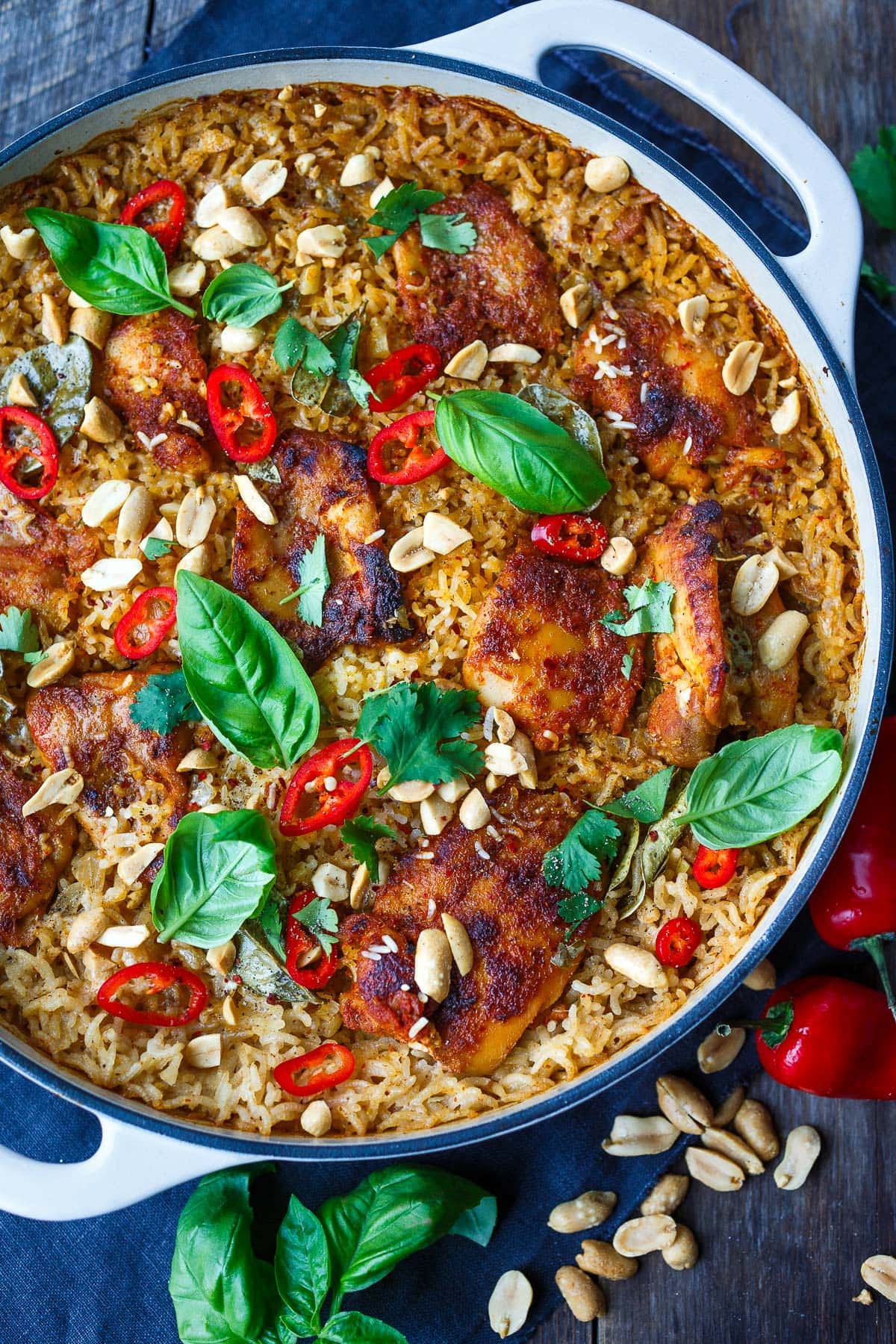 baked chicken and rice with thai red curry- in dutch oven with coconut rice, red chilis, peanuts, basil, and cilantro garnish.