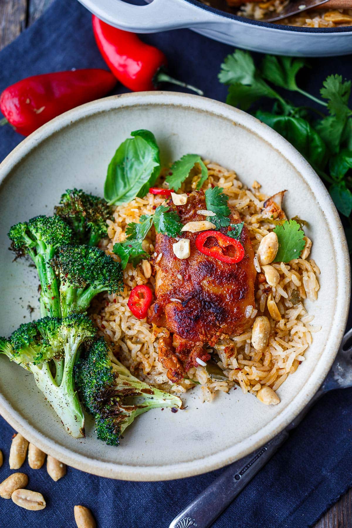 baked red curry chicken and rice on plate with roasted broccoli, garnished with red chilis, basil, cilantro, and peanuts.