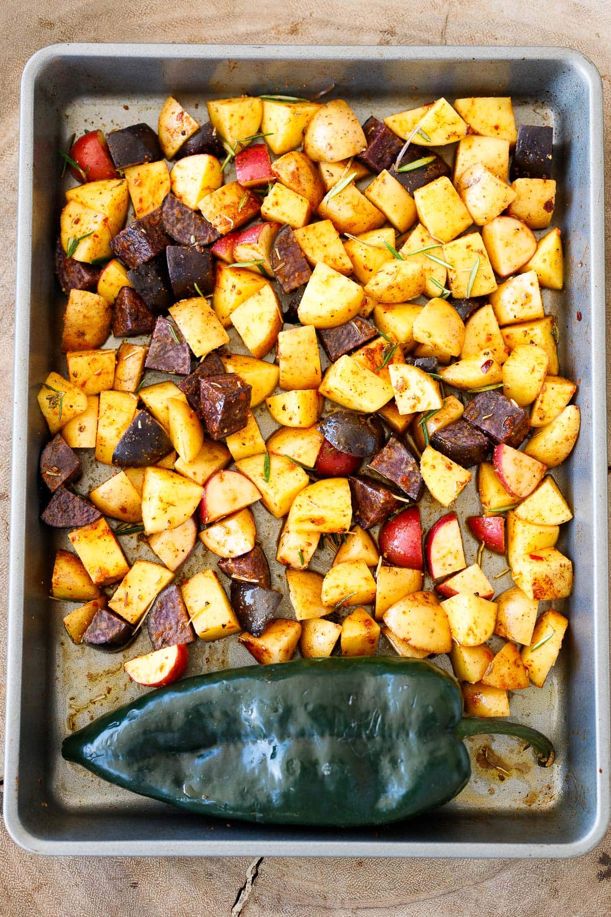 diced potatoes on sheet pan with spices and herbs, beside whole poblano pepper.