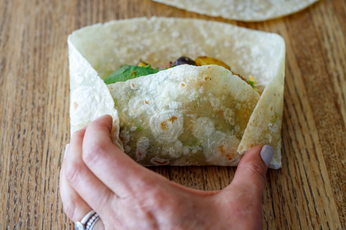 folding breakfast burrito with hands, bottom edge folded over center with edges tucked in.