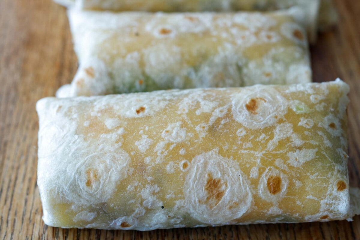 wrapped breakfast burritos seam side down on cutting board.