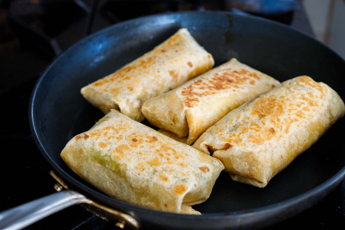 toasted breakfast burritos in skillet seam side down.