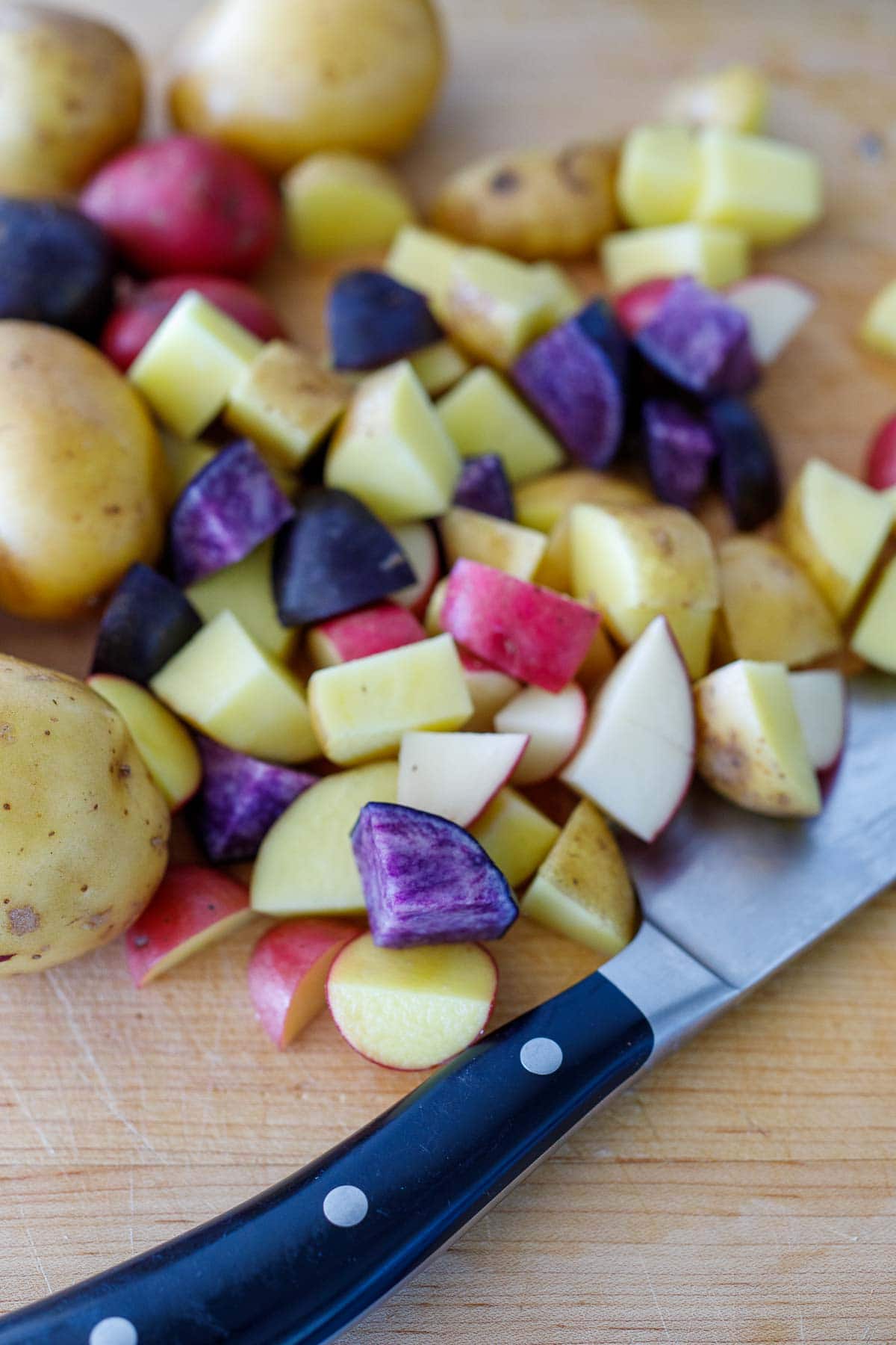 knife and cutting board chopping potatoes into 3/4 inch cubes.