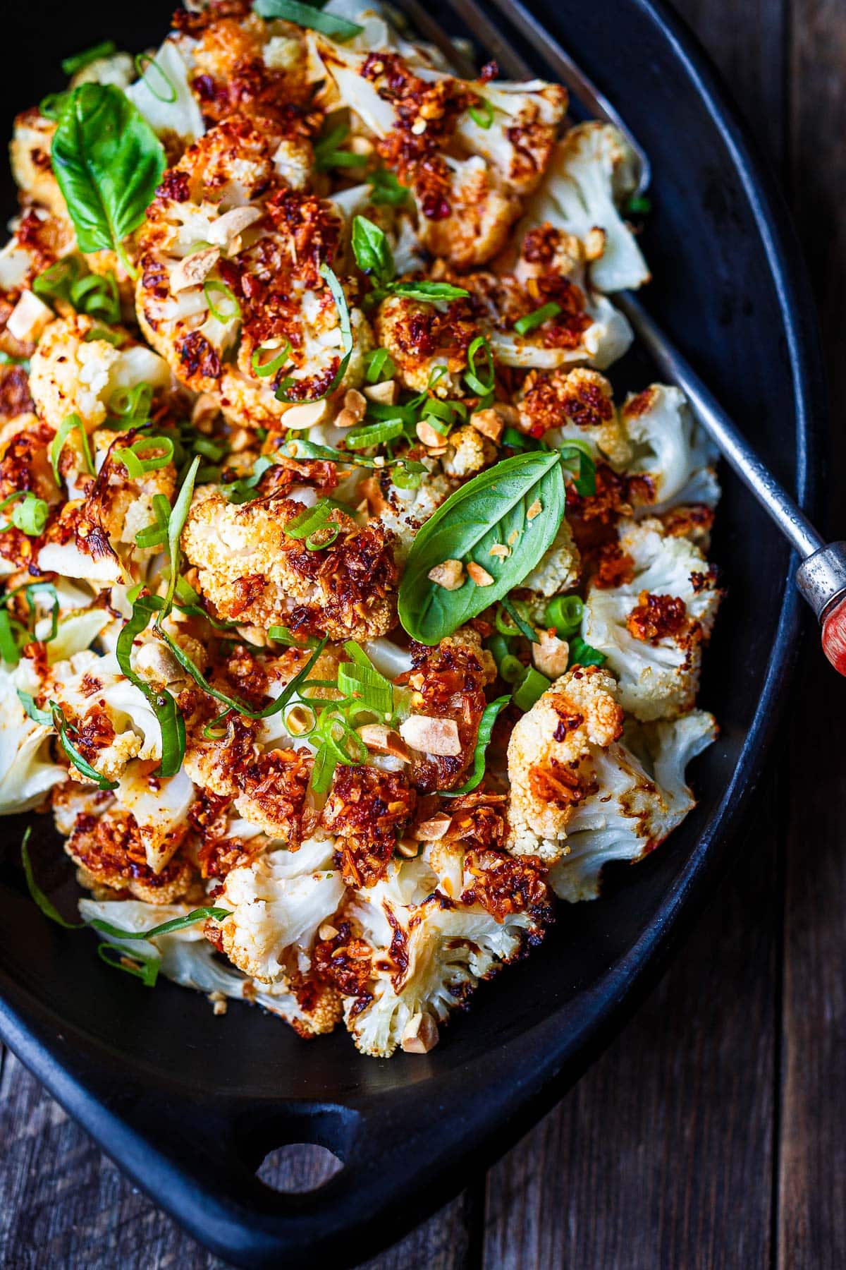 chili crisp cauliflower in a serving bowl garnished with basil, scallions, peanuts.