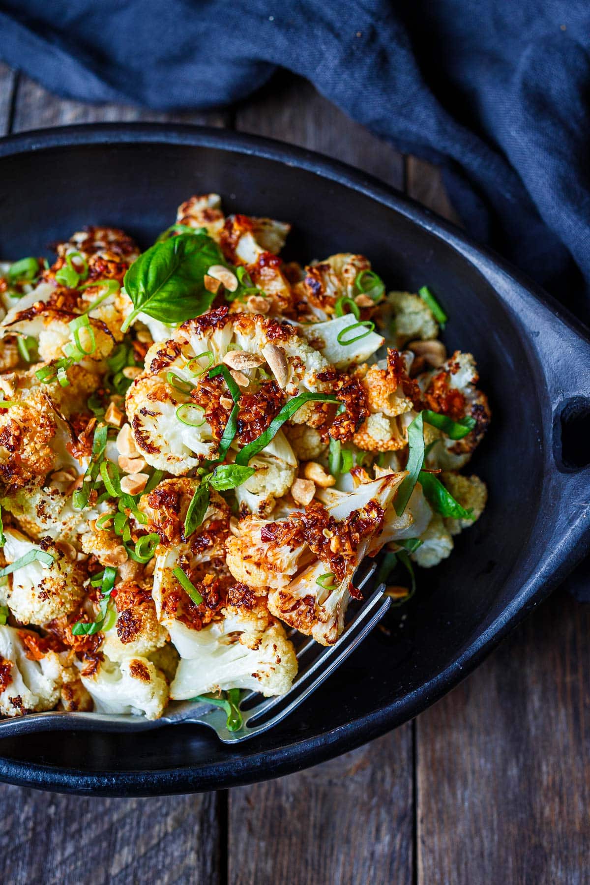 chili crisp cauliflower in serving bowl made with homemade chili crisp, garnished with basil, scallions, and peanuts.