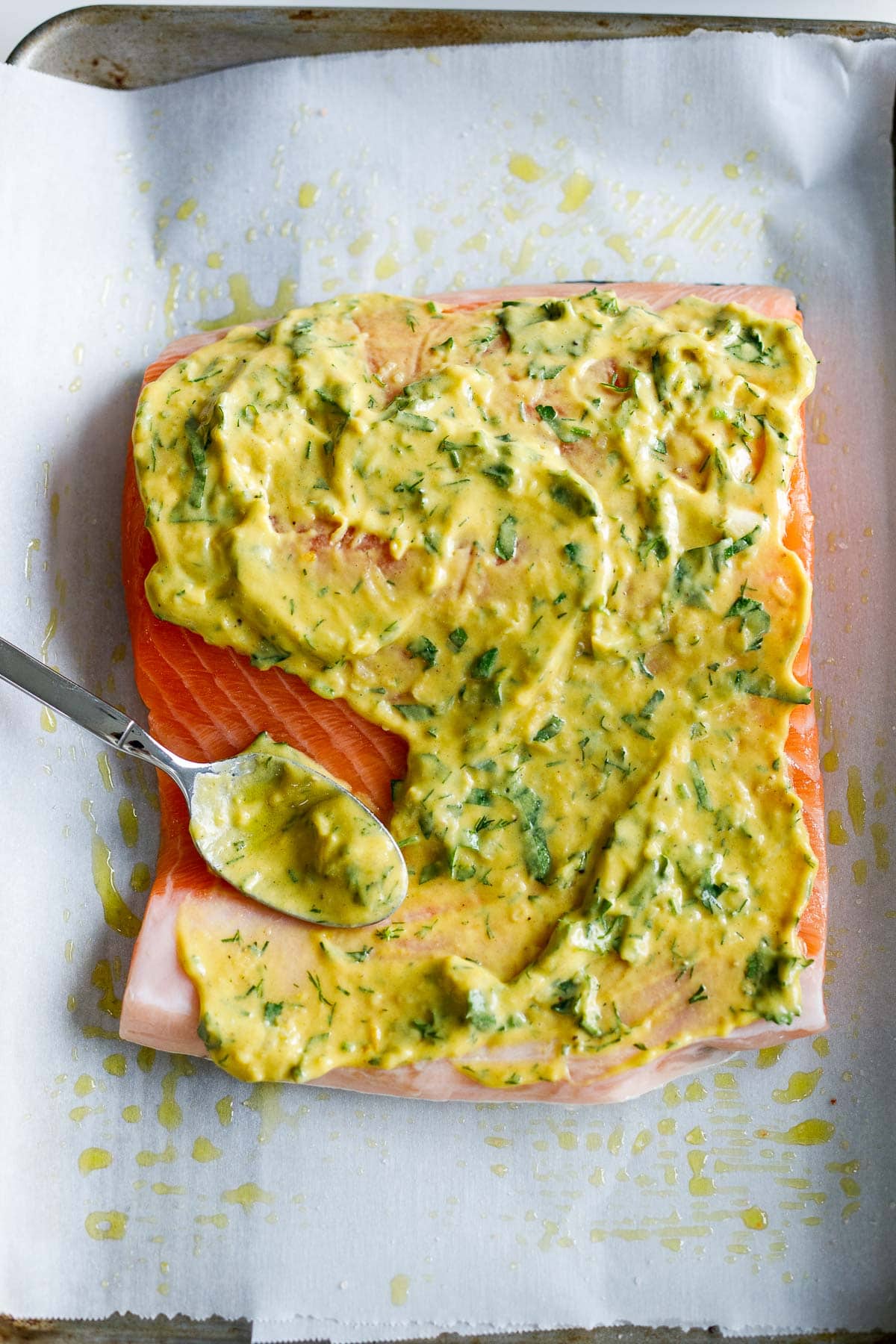 spreading herby dijon mixture over salmon with spoon.