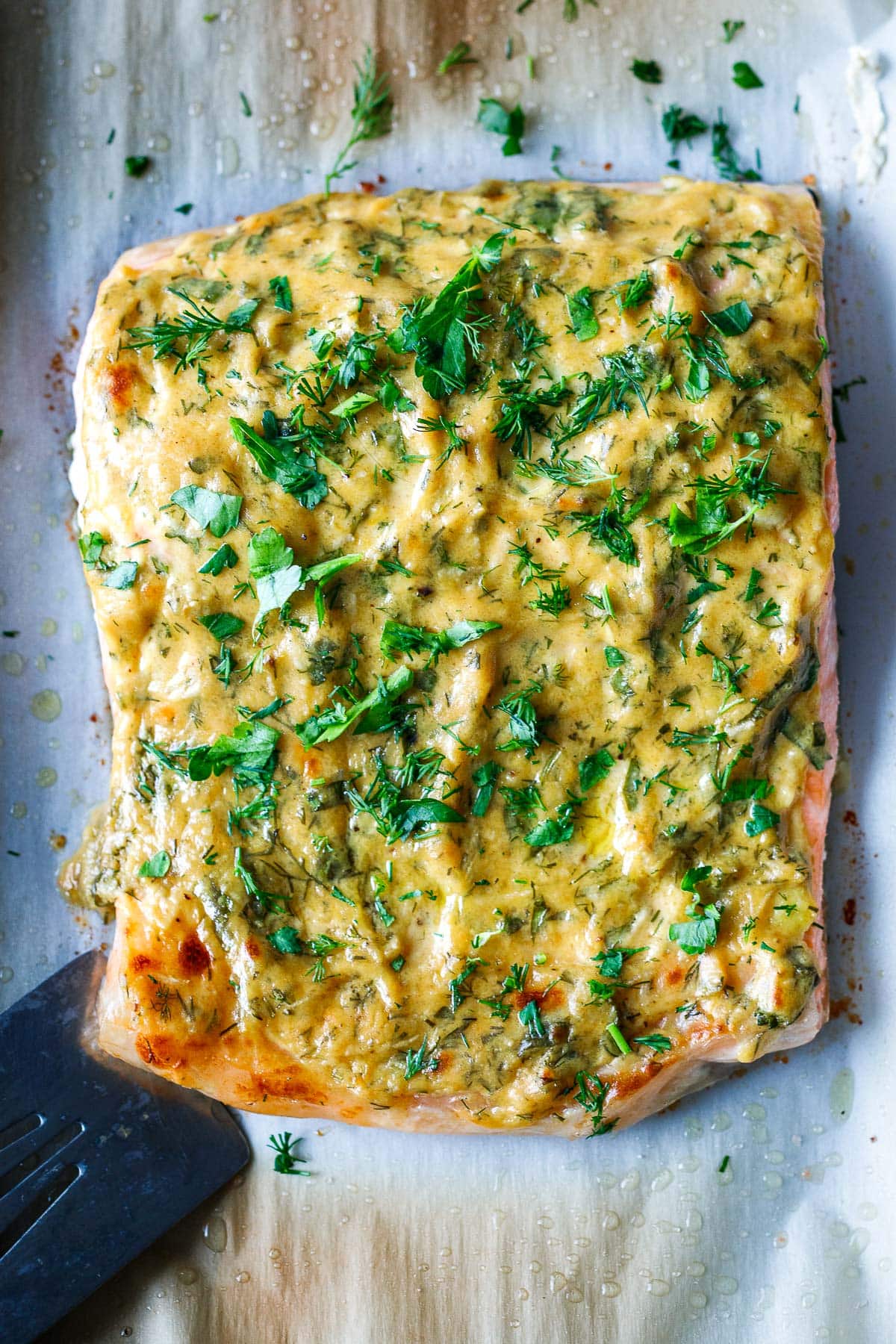 baked dijon salmon on baking sheet with broiled top, garnished with fresh herbs.