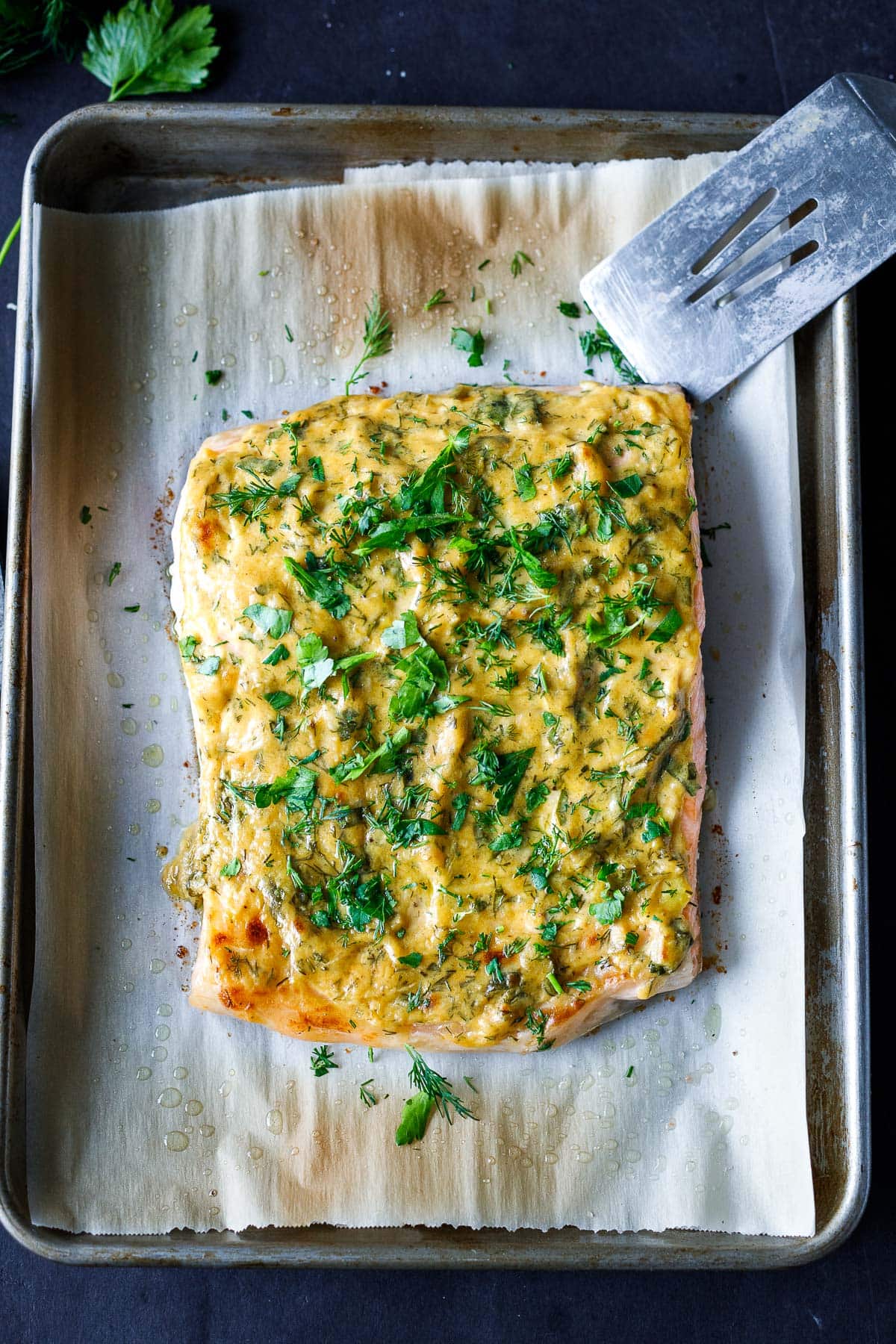 baked dijon salmon on parchment lined baking sheet, covered in dijon marinade with fresh herbs.