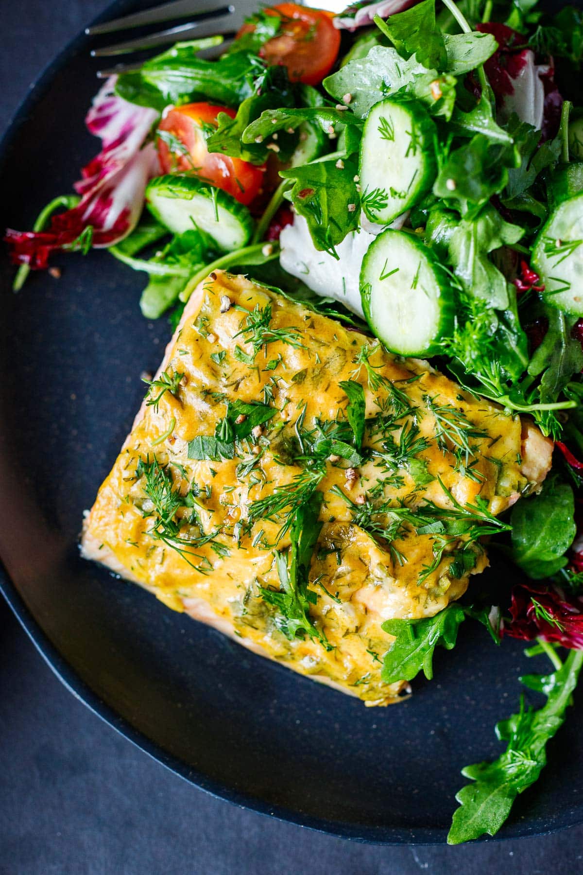 baked dijon salmon on plate with green salad, garnished with fresh herbs.