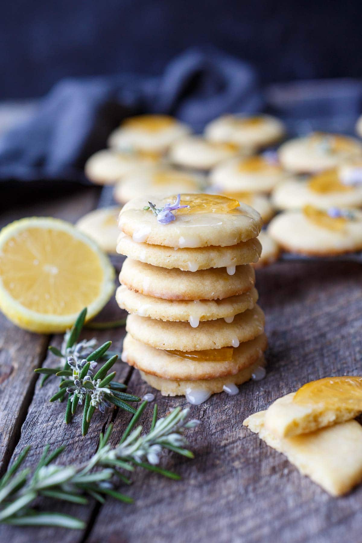 stack of lemon cookies dripping in lemon glaze, garnished with candied lemon and rosemary flower.