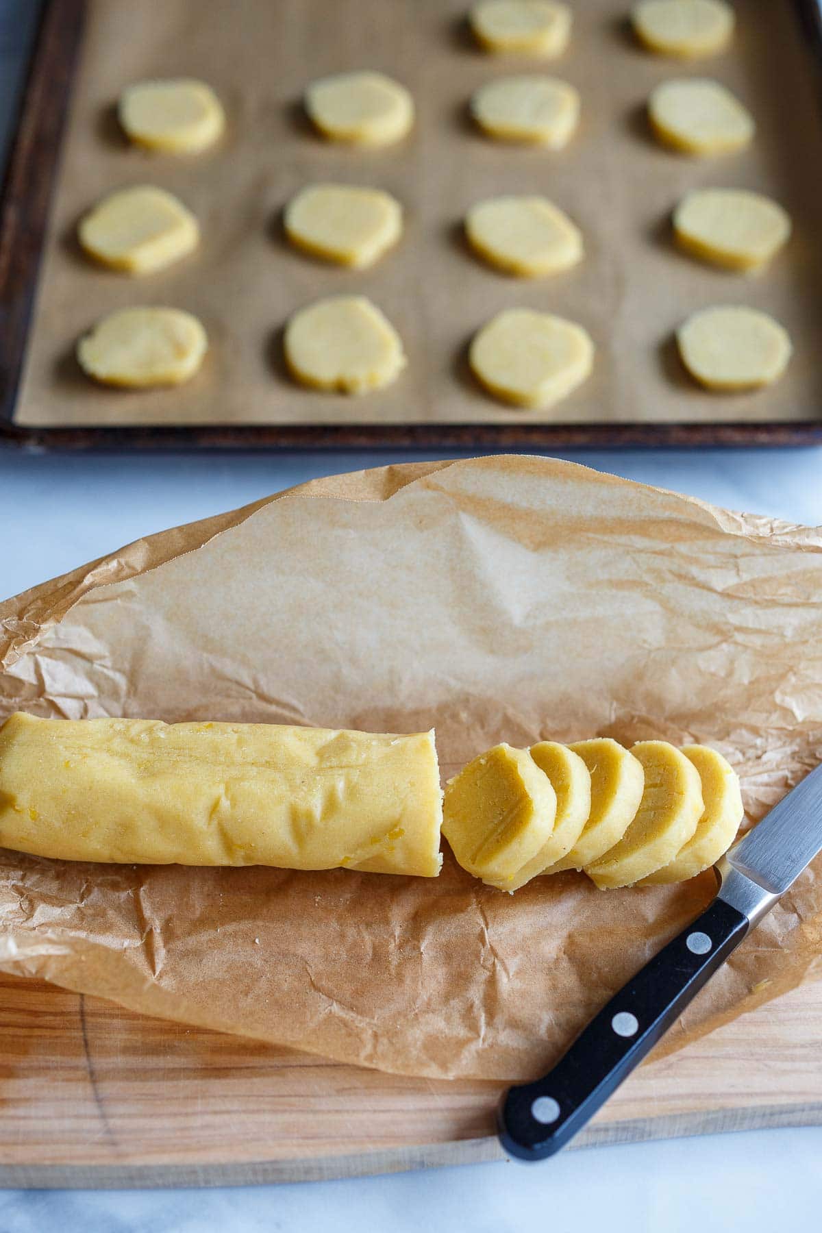 knife slicing cookie shapes from roll of lemon cookie batter.