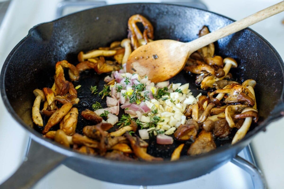 cast iron skillet with sautéed mushrooms with well in center where garlic and shallots and thyme are added.