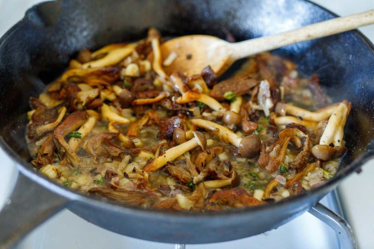 sautéed mushrooms cooking with shallot, garlic, and herbs in oil in skillet.