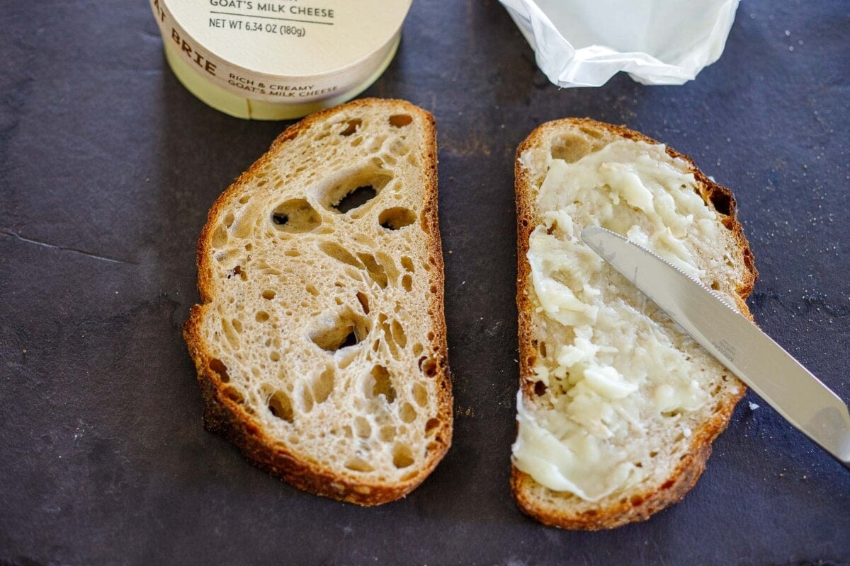 spreading goat cheese on slice of sourdough bread.