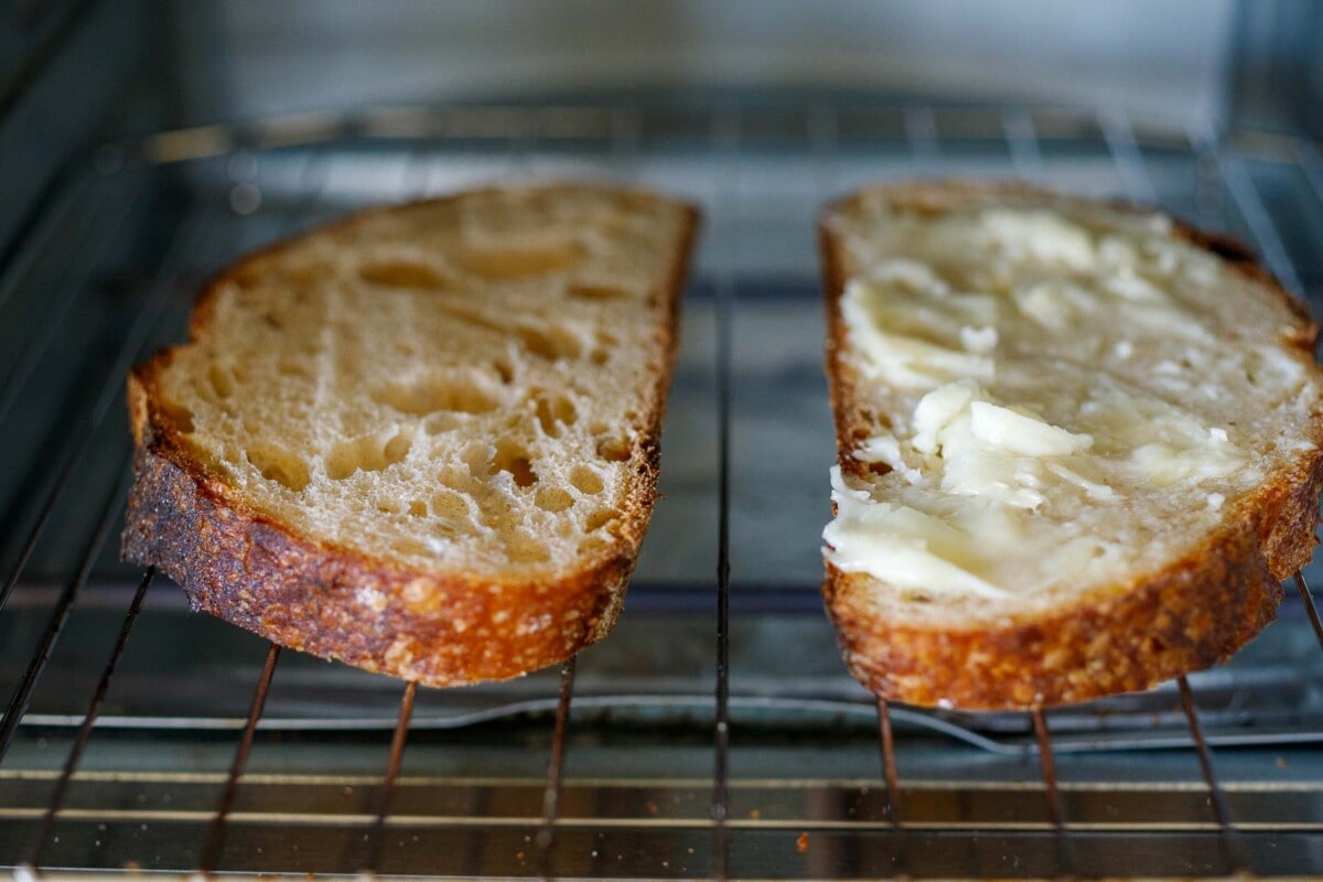 sourdough slices toasting in toaster oven, one with layer of goat cheese.