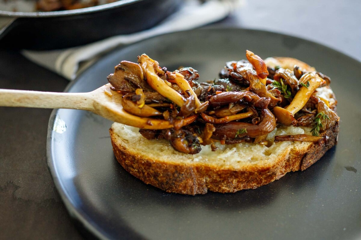 wood spoon piling mushrooms on top of toasted bread.