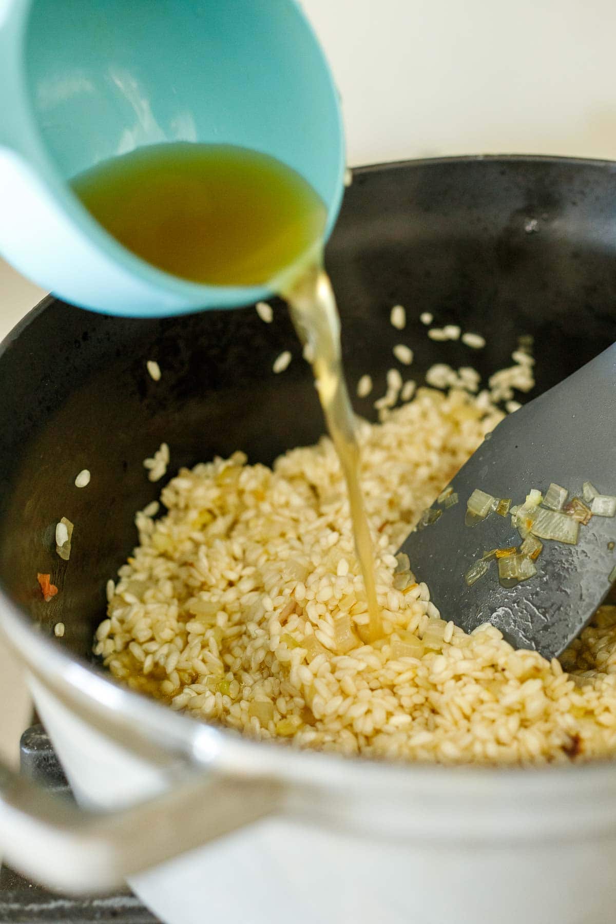 pouring hot vegetable broth into dutch oven with arborio rice to make risotto.