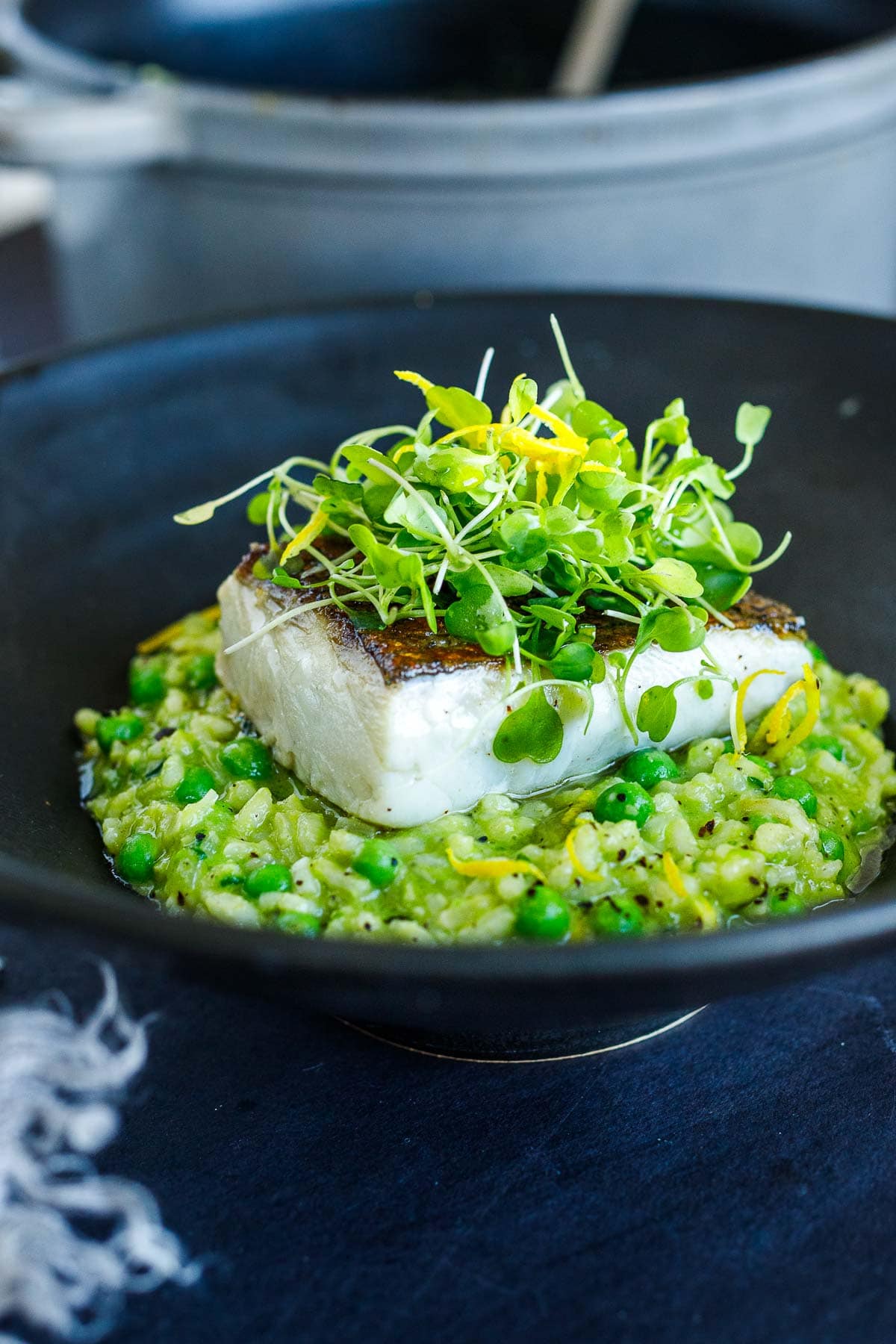 serving bowl with spring pea risotto, pan-seared white fish, garnished with microgreens and lemon zest.