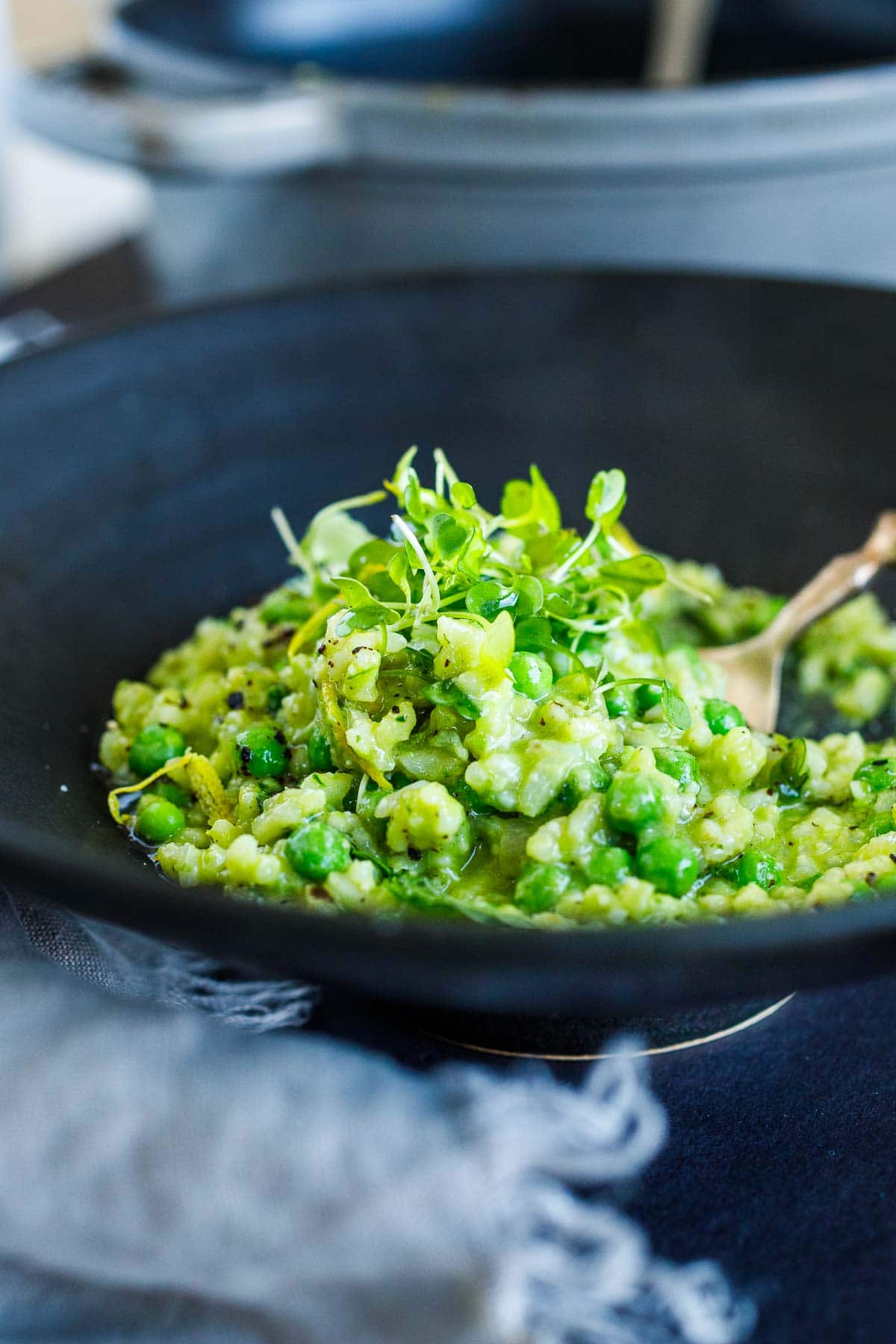 serving bowl with spring pea risotto with fresh peas, lemon zest, and microgreens for garnish.