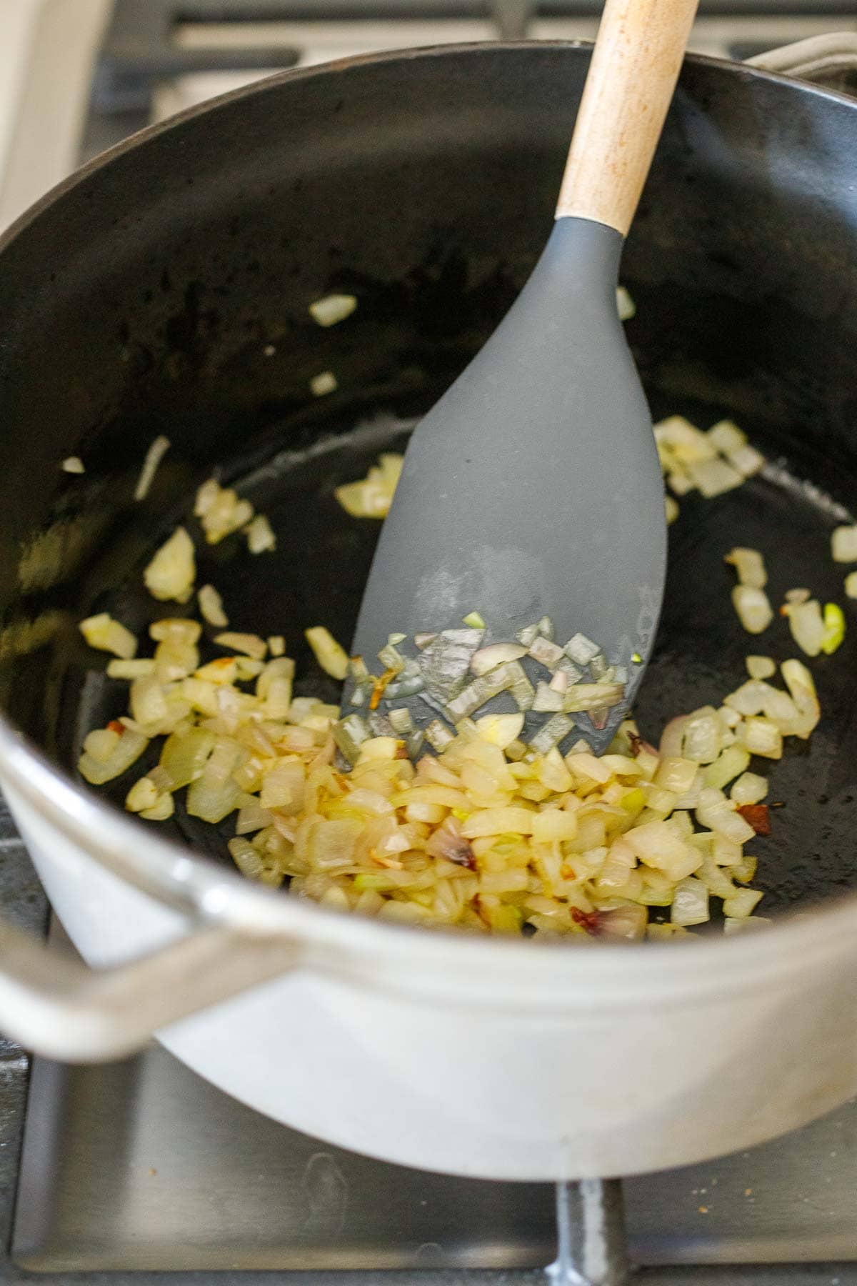 diced onions and garlic sautéing in dutch oven with silicone spatula. 