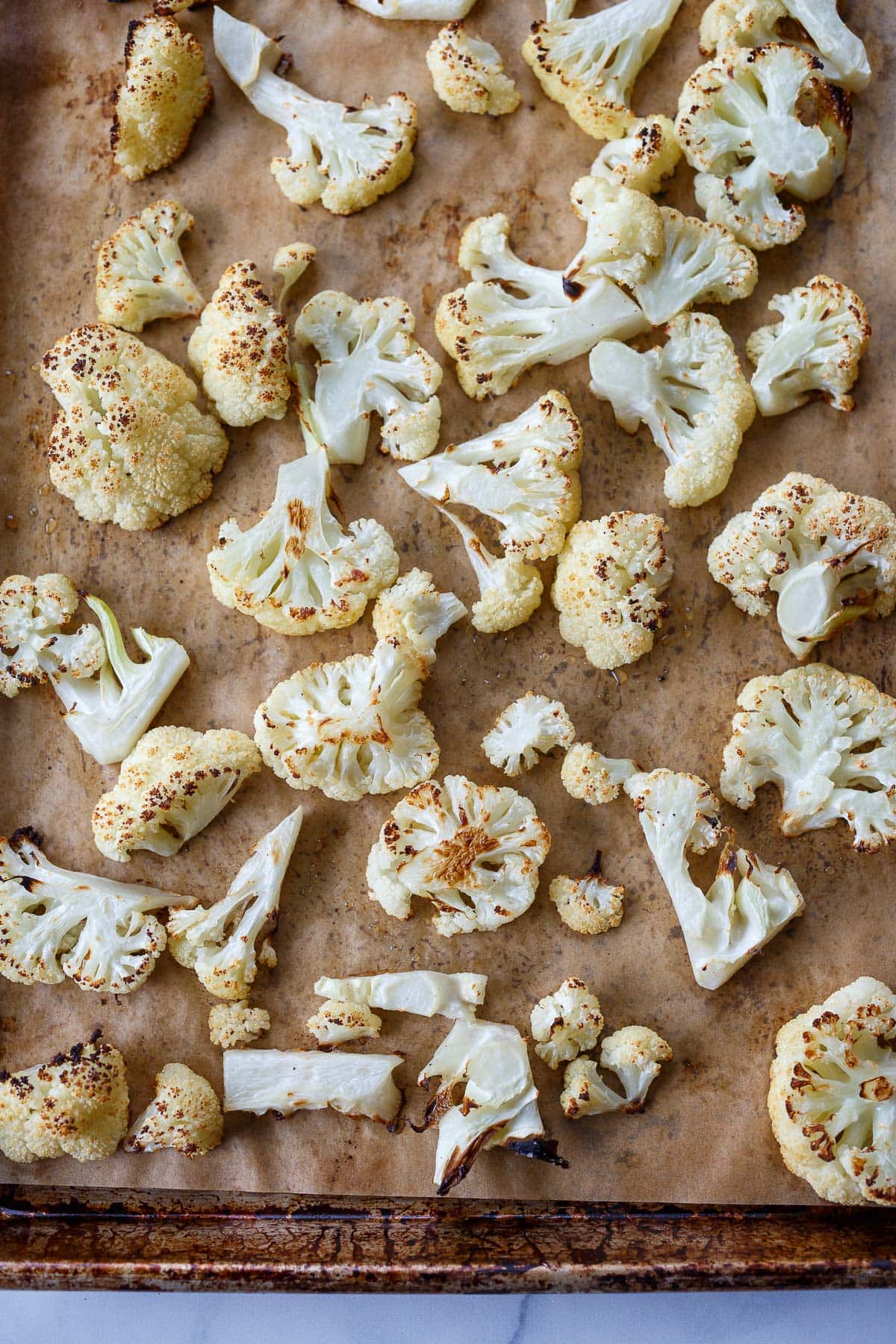 roasted cauliflower spread out on parchment-lined baking sheet, perfectly browned.
