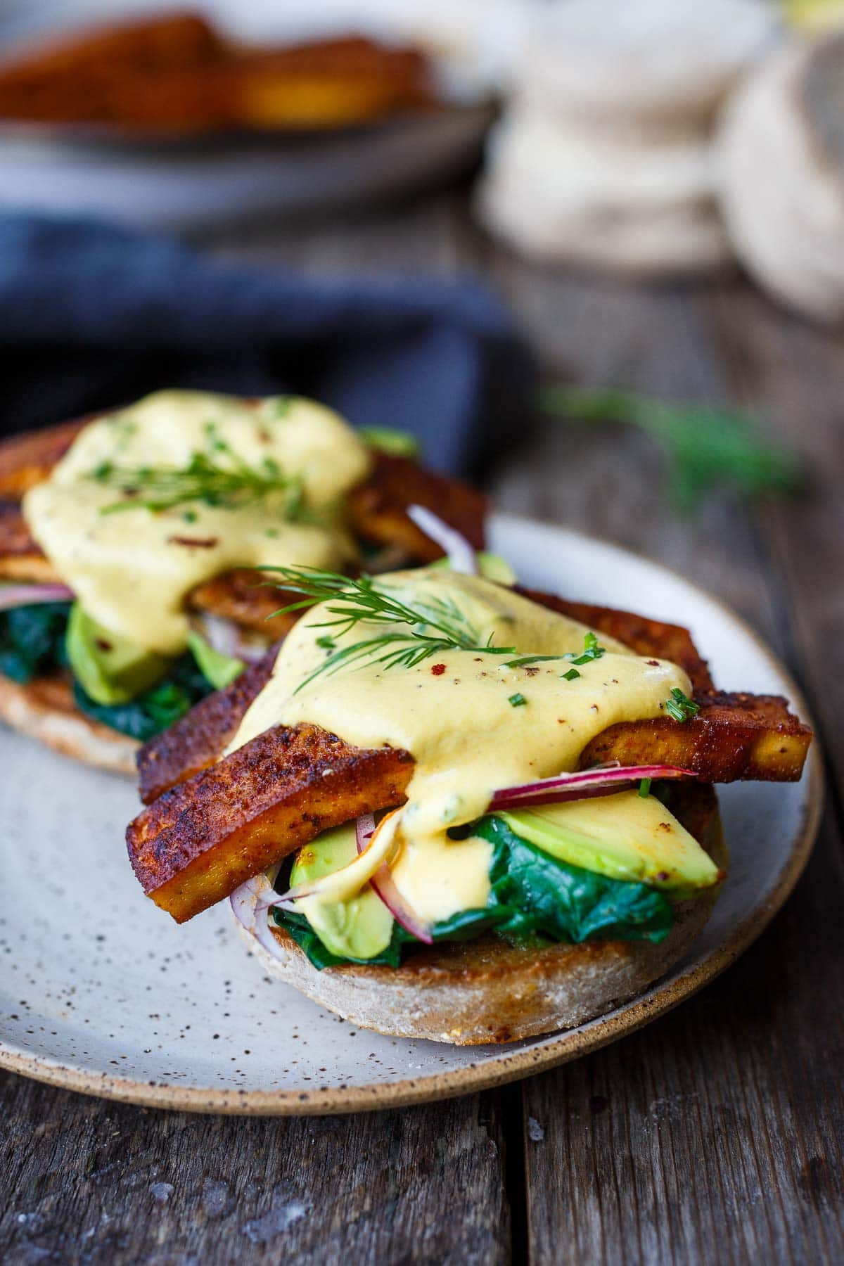 vegan eggs benedict with vegan hollandaise, tofu bacon, red onion, avocado, wilted spinach on toasted english muffin.