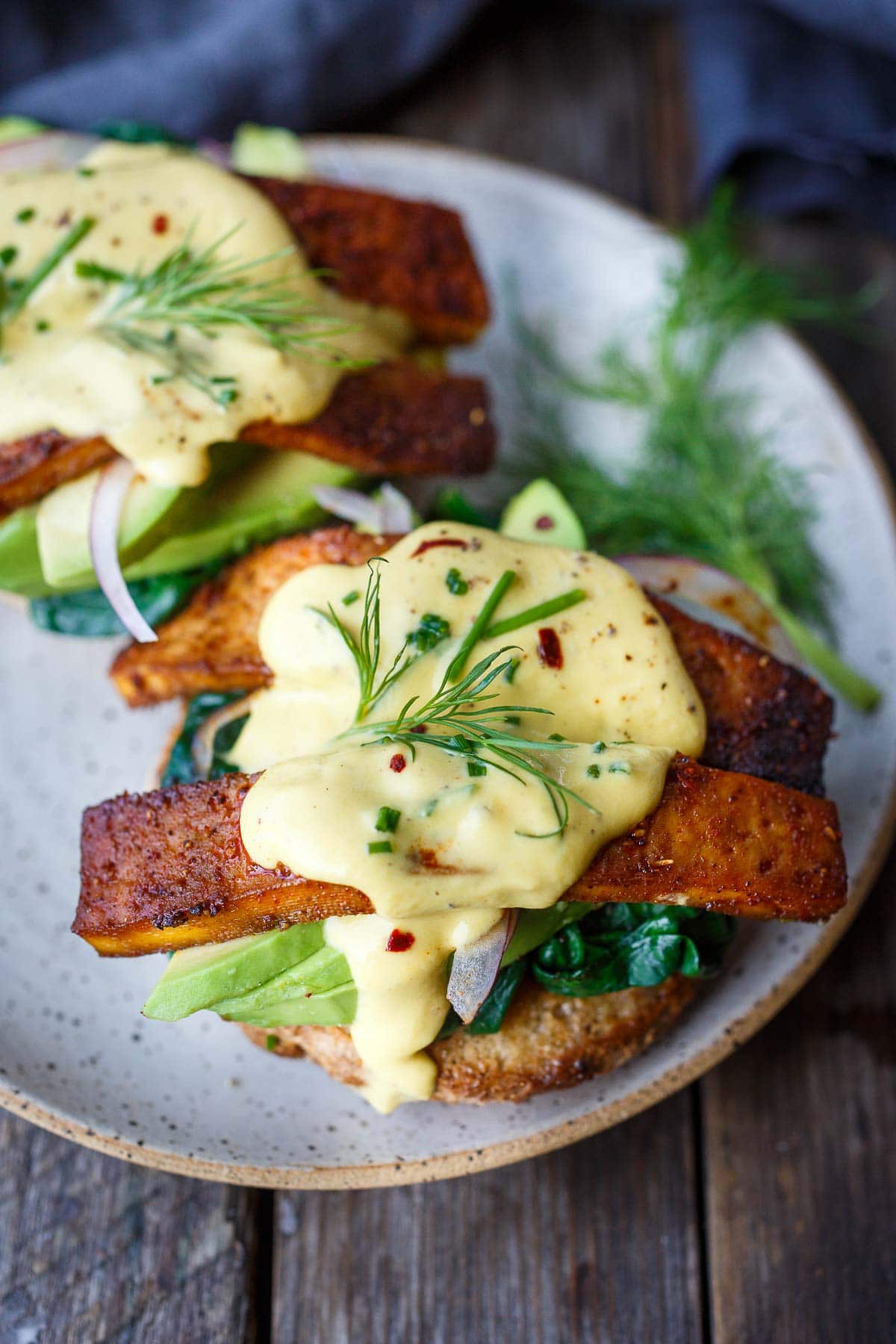 vegan eggs benedict with vegan hollandaise sauce, tofu bacon, avocado, spinach on sourdough english muffin.