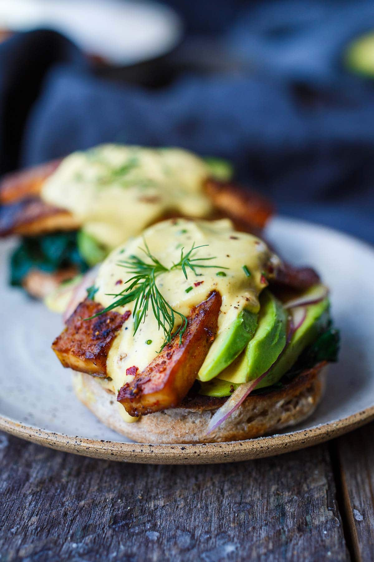vegan eggs benedict with tofu bacon and vegan hollandaise sauce, made with avocado and red onion, garnished with dill.
