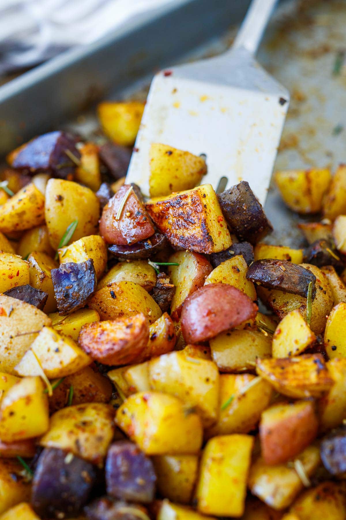 easy breakfast potatoes, roasted and well seasoned with spices and herbs, on baking sheet with metal spatula.