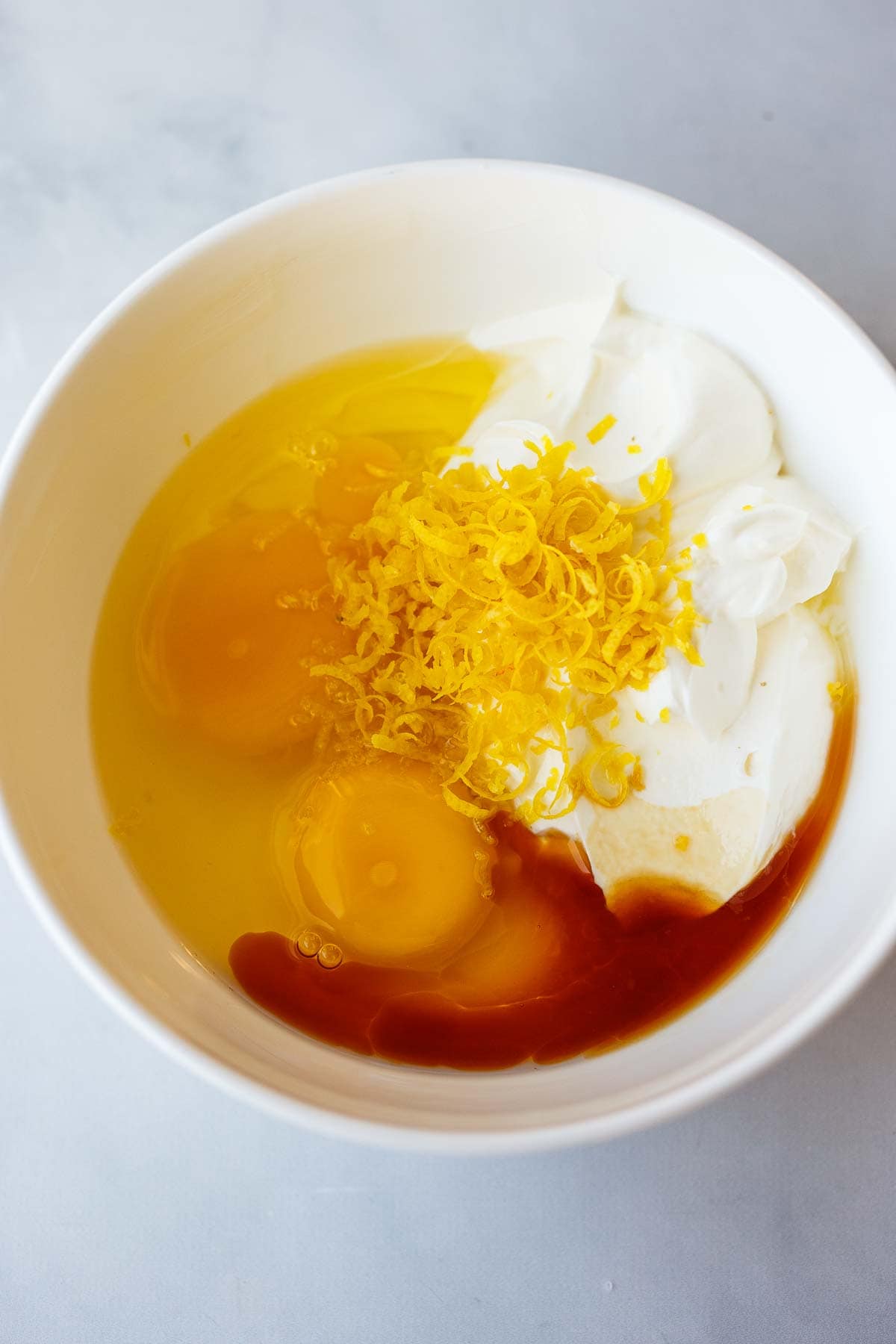 small bowl with eggs, sour cream, oil, milk, vanilla, and lemon zest.