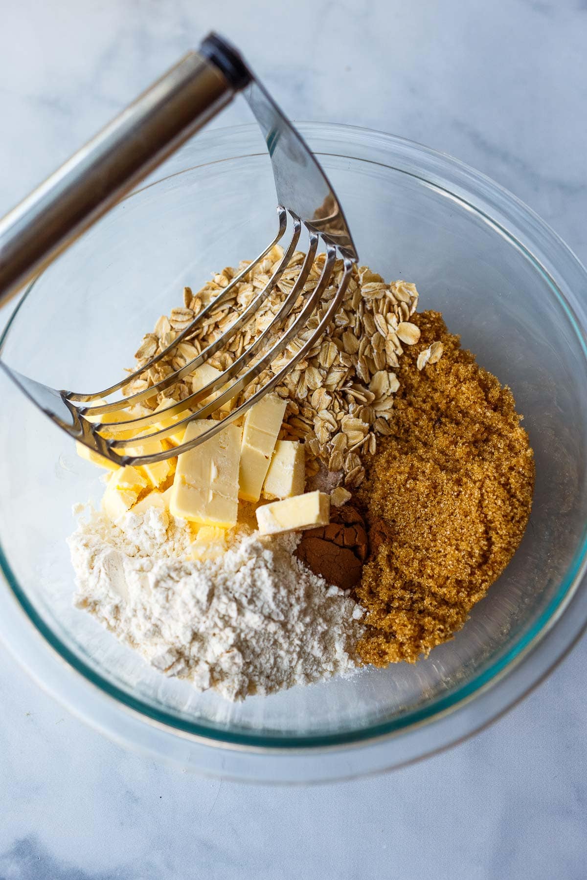 pastry cutter in mixing bowl with oats, brown sugar, cinnamon, butter, and flour.