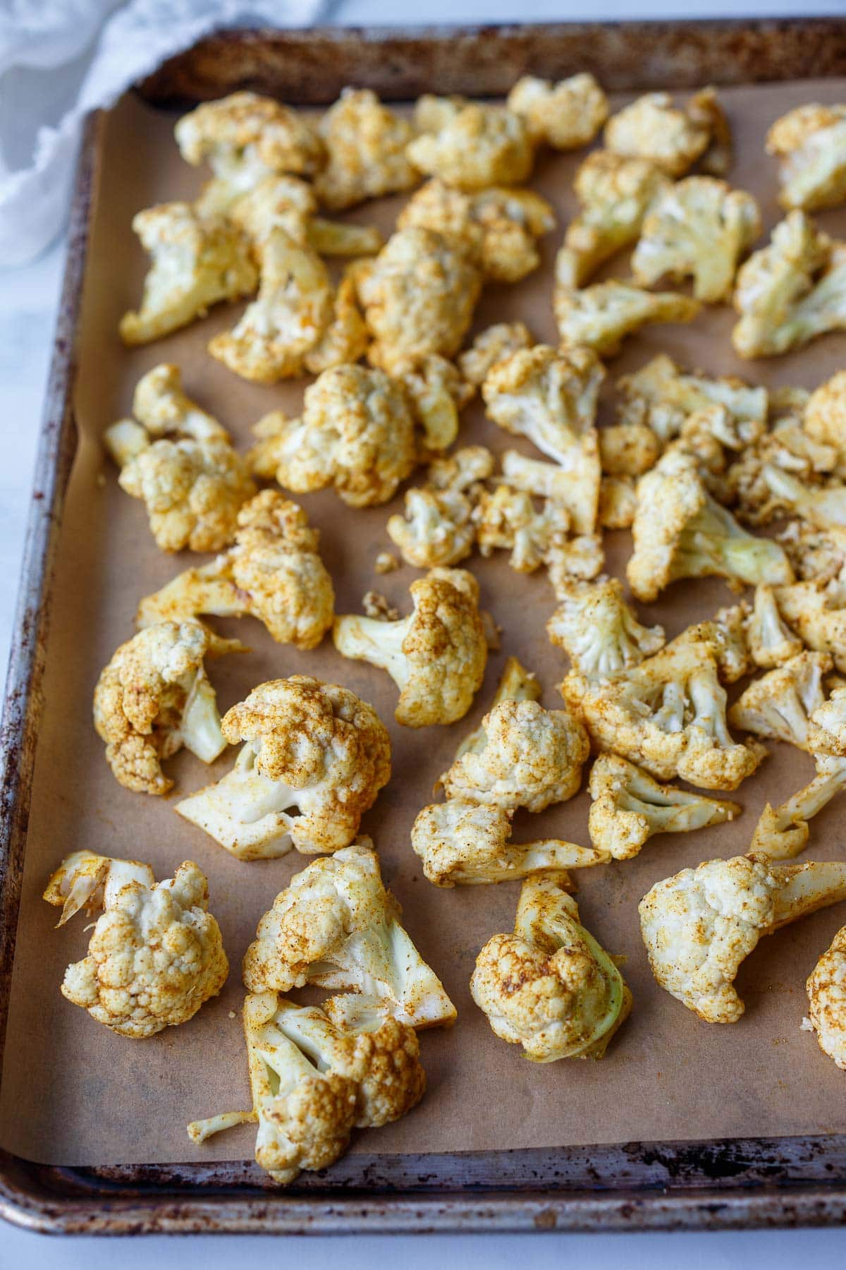 cauliflower florets on parchment-lined baking sheet seasoned with shawarma spice blend.