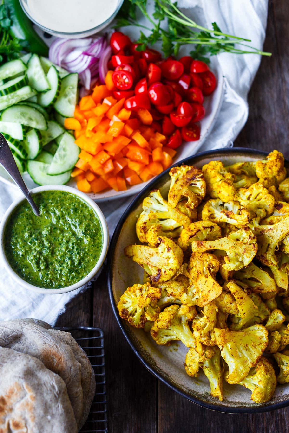 roasted cauliflower shawarma in bowl with serving optoins - tahini, zhoug, chopped veggies, and pita.