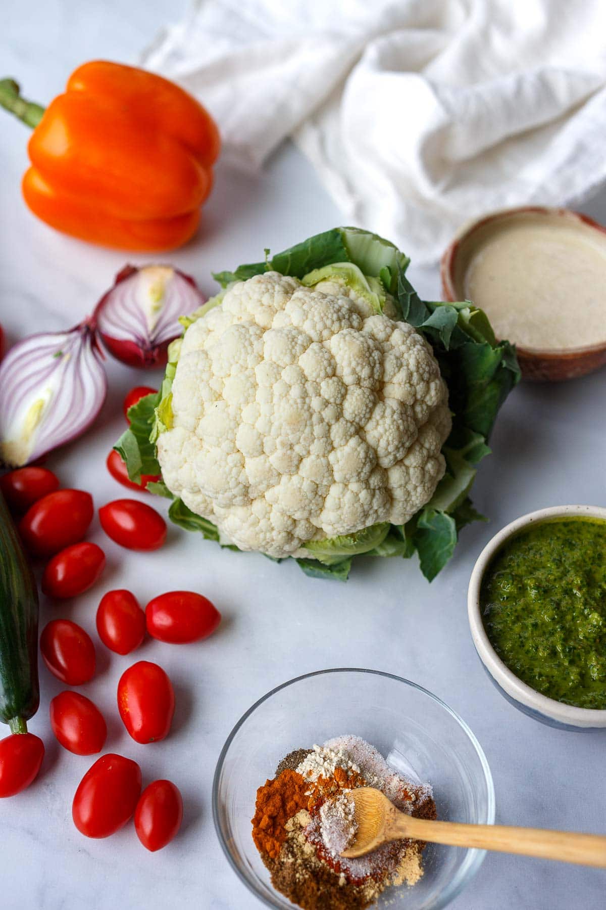ingredients for cauliflower shawarma- cauliflower head, onion, tomato, cucumber, tahini sauce, zhoug, shawarma spice blend.