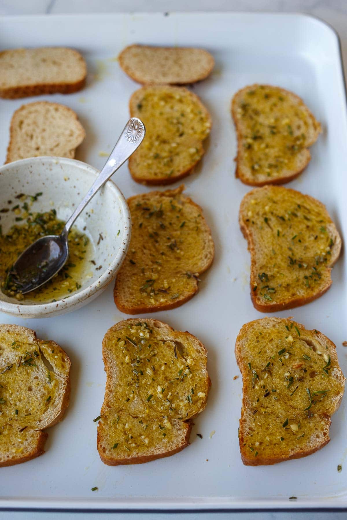 baking sheet with sourdough slices rubbed in oil, garlic, rosemary mixture.