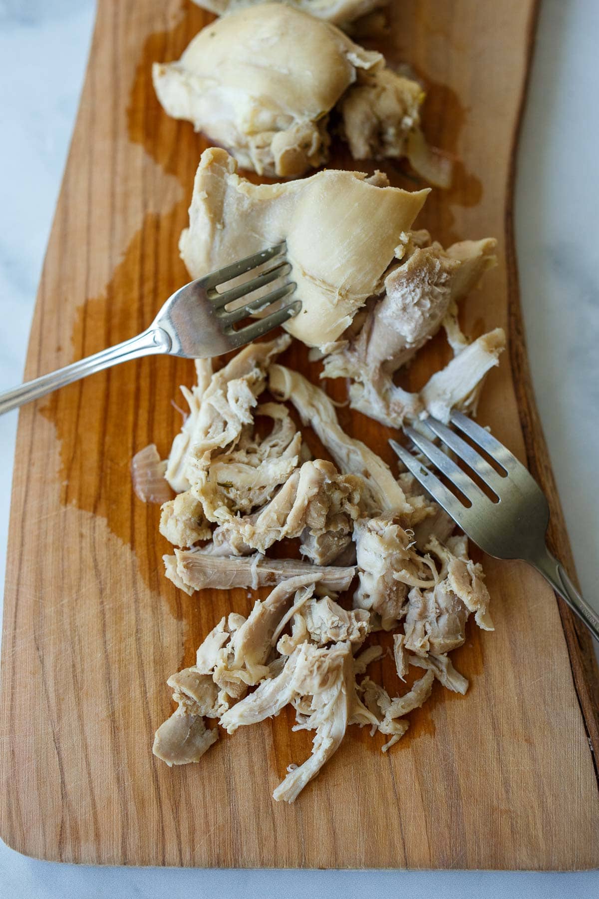 forks shredding chicken on wood board.