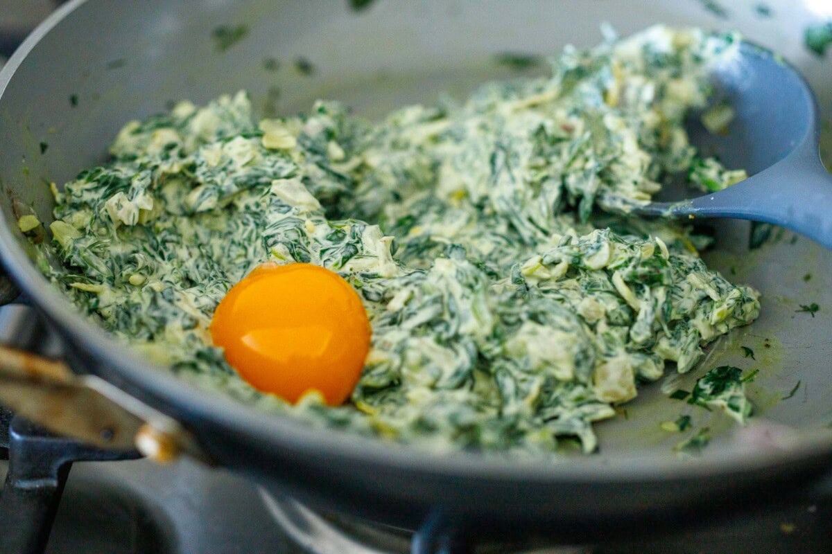 skillet with cream cheese and spinach mixture and egg yolk added.