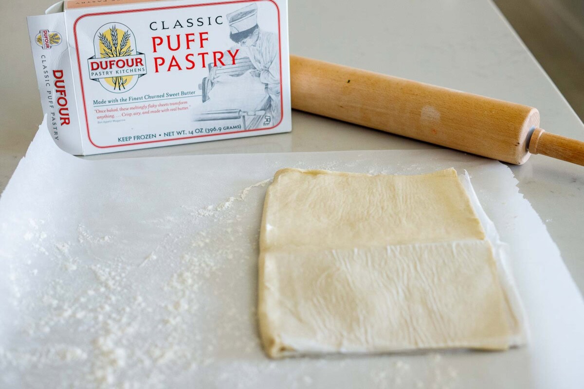 puff pastry laid out on floured parchment paper beside rolling pin.