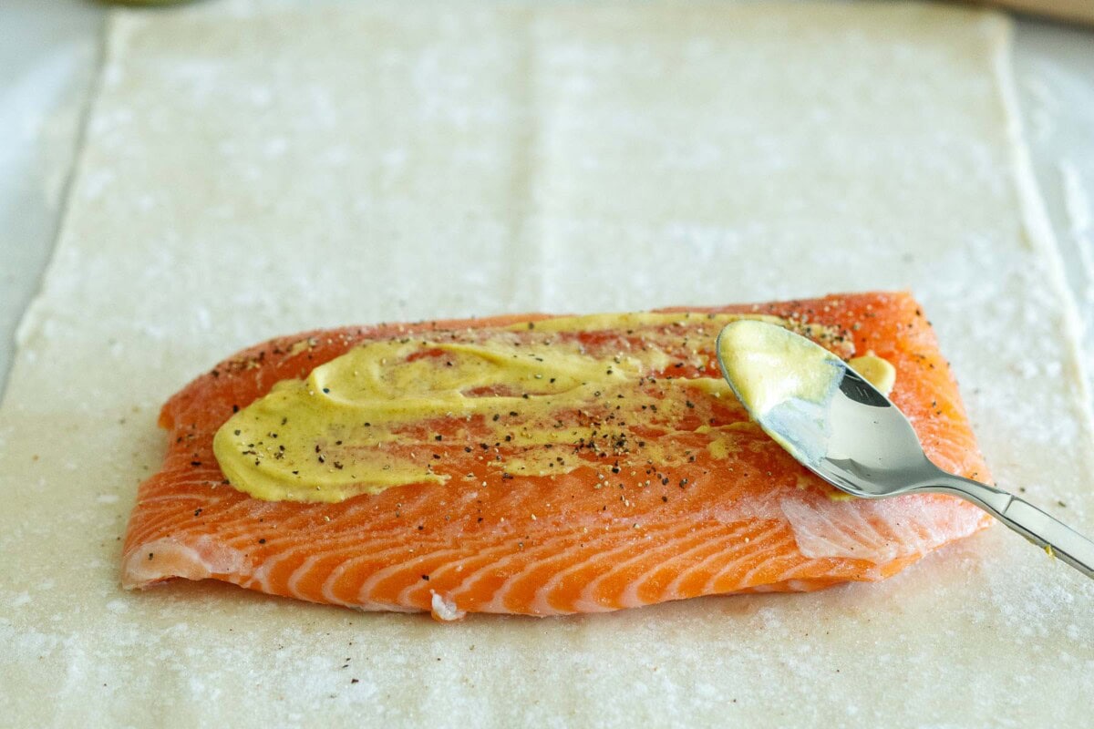 spoon spreading dijon mustard over salmon.