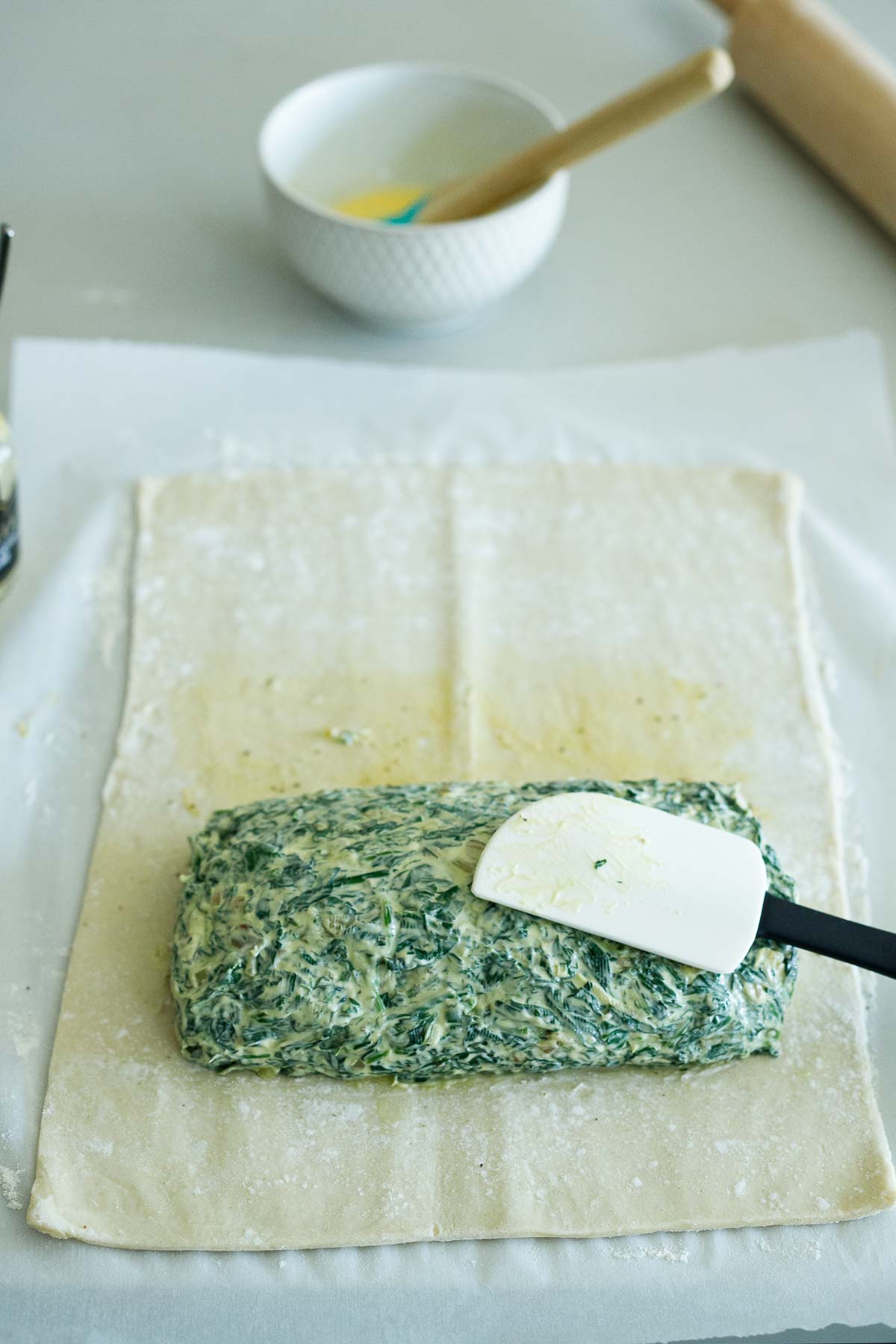 rubber spatula spreading creamy spinach filling around all edges of the salmon, smoothing it out.
