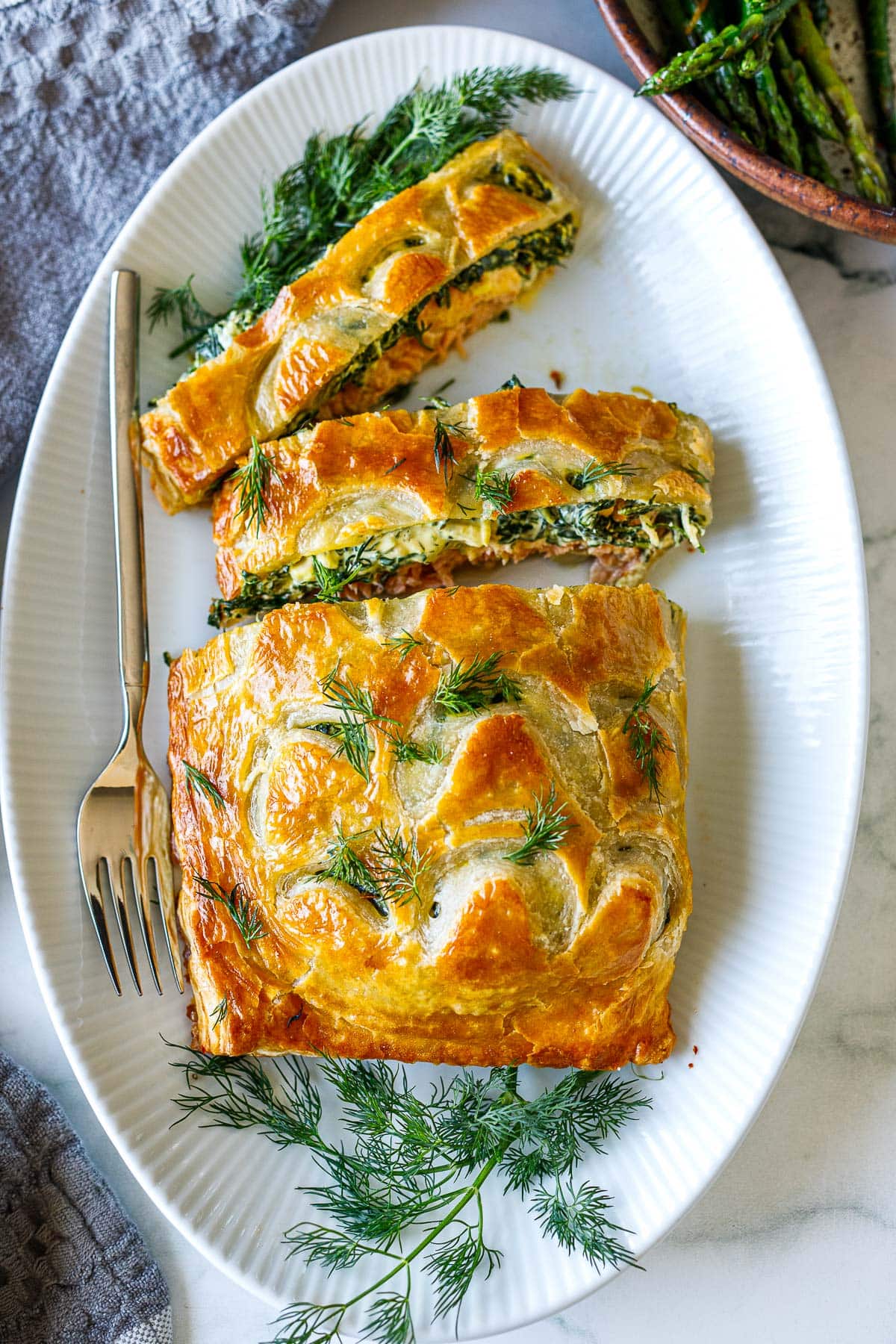 salmon wellington with fresh dill on serving platter, cut into slices.