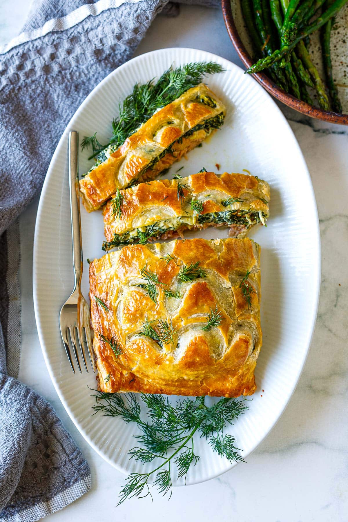 salmon wellington on serving platter with two slices cut, garnished with fresh dill.