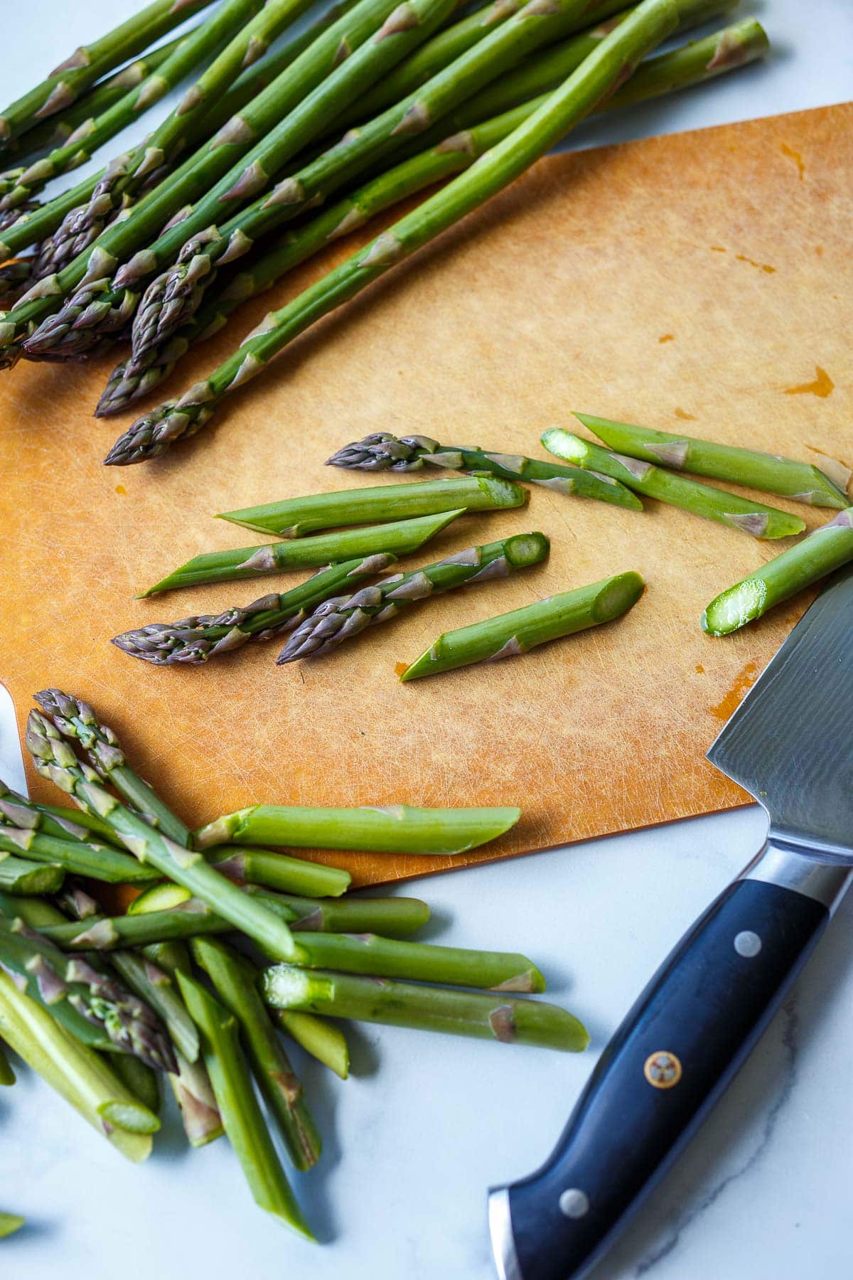 sharp knife cutting asparagus bunch into diagonal julienne pieces.