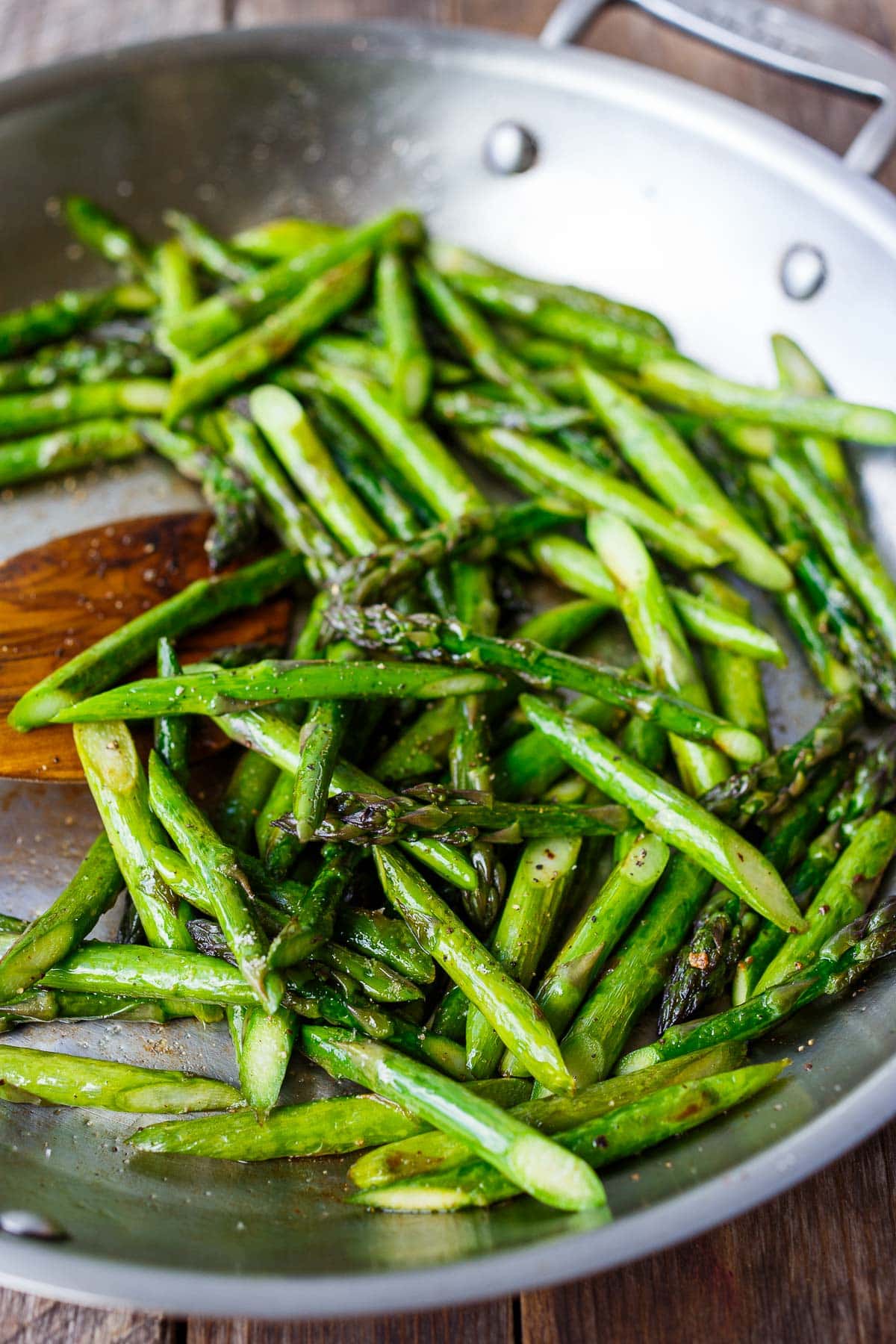 wood spoon stirring sauteed asparagus in skillet.