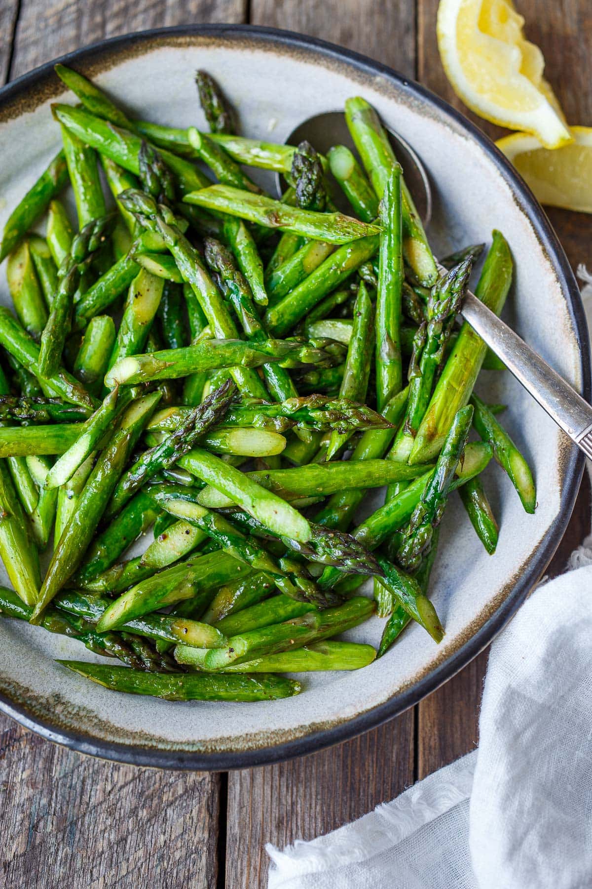 serving bowl with bright green sauteed asparagus seasoned with salt and pepper.
