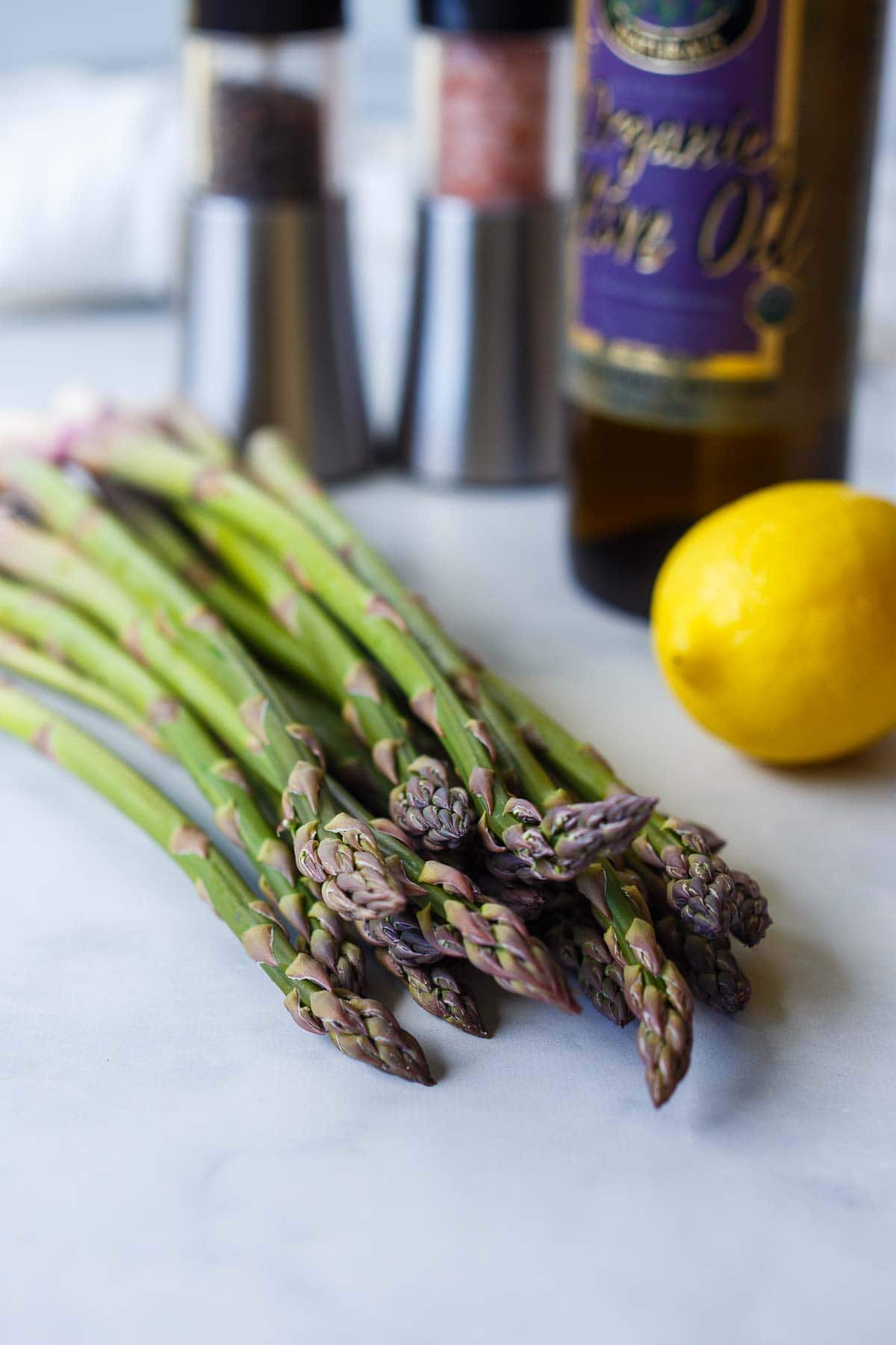 fresh asparagus bunch on counter with lemon, olive oil, and salt and pepper shakers.