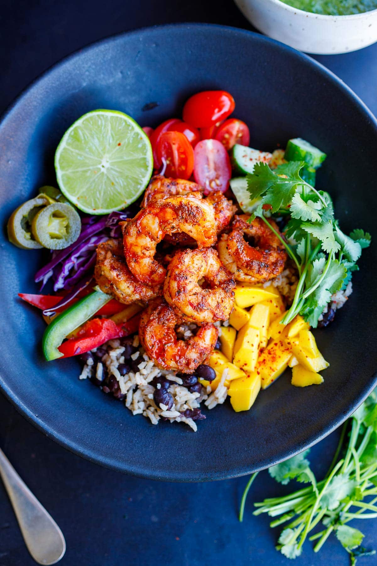 spicy Mexican shrimp bowl with rice and beans, mango, cilantro, cucumber, tomato, lime, pickled jalapeno, cabbage, and bell peppers.