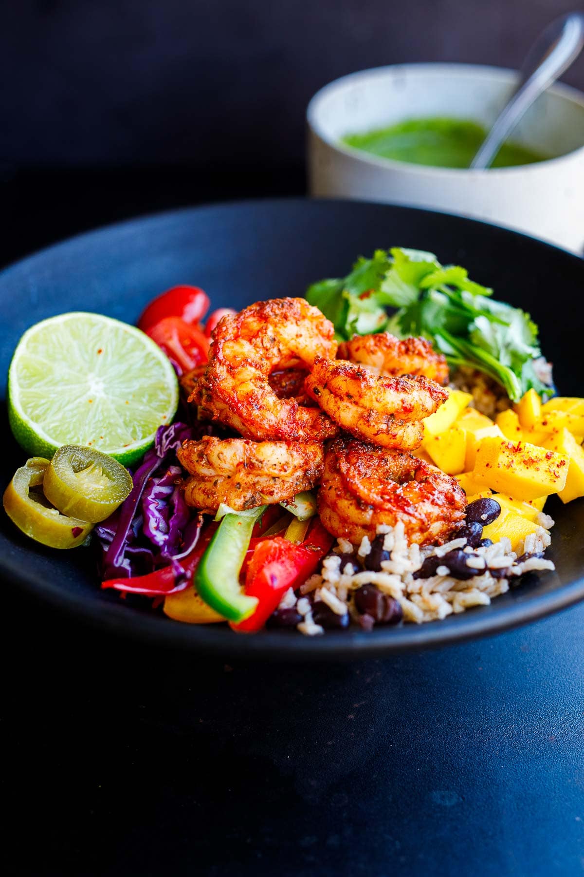 spicy Mexican shrimp in rice and bean bowl with mango, bell peppers, cabbage, pickled jalapeño, lime, cilantro, tomatoes.