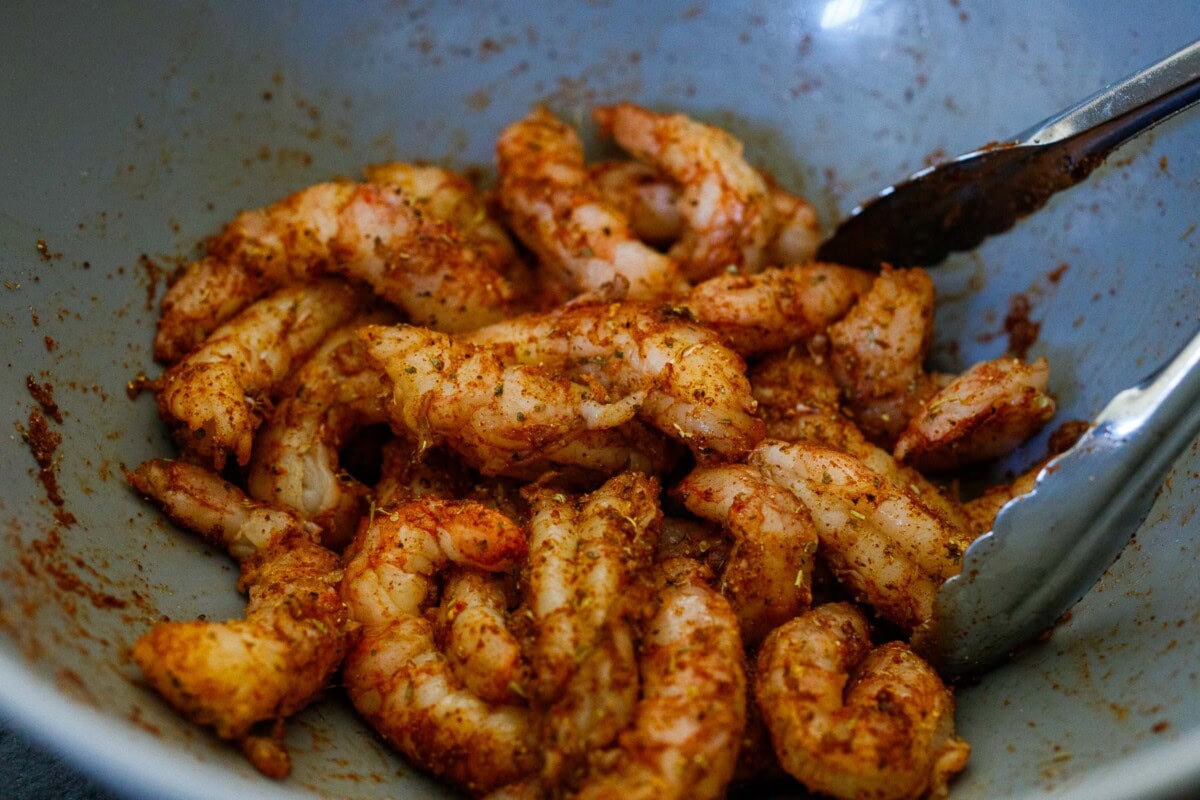 tongs mixing shrimp in spicy Mexican seasoning.